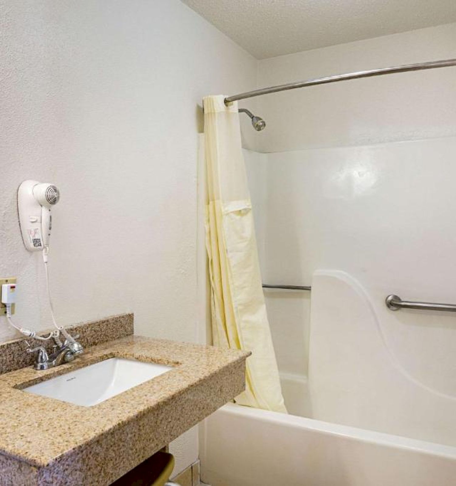 The image shows a bathroom with a sink, counter, mounted hairdryer, mirror, and a bathtub with a shower curtain and grab bar.