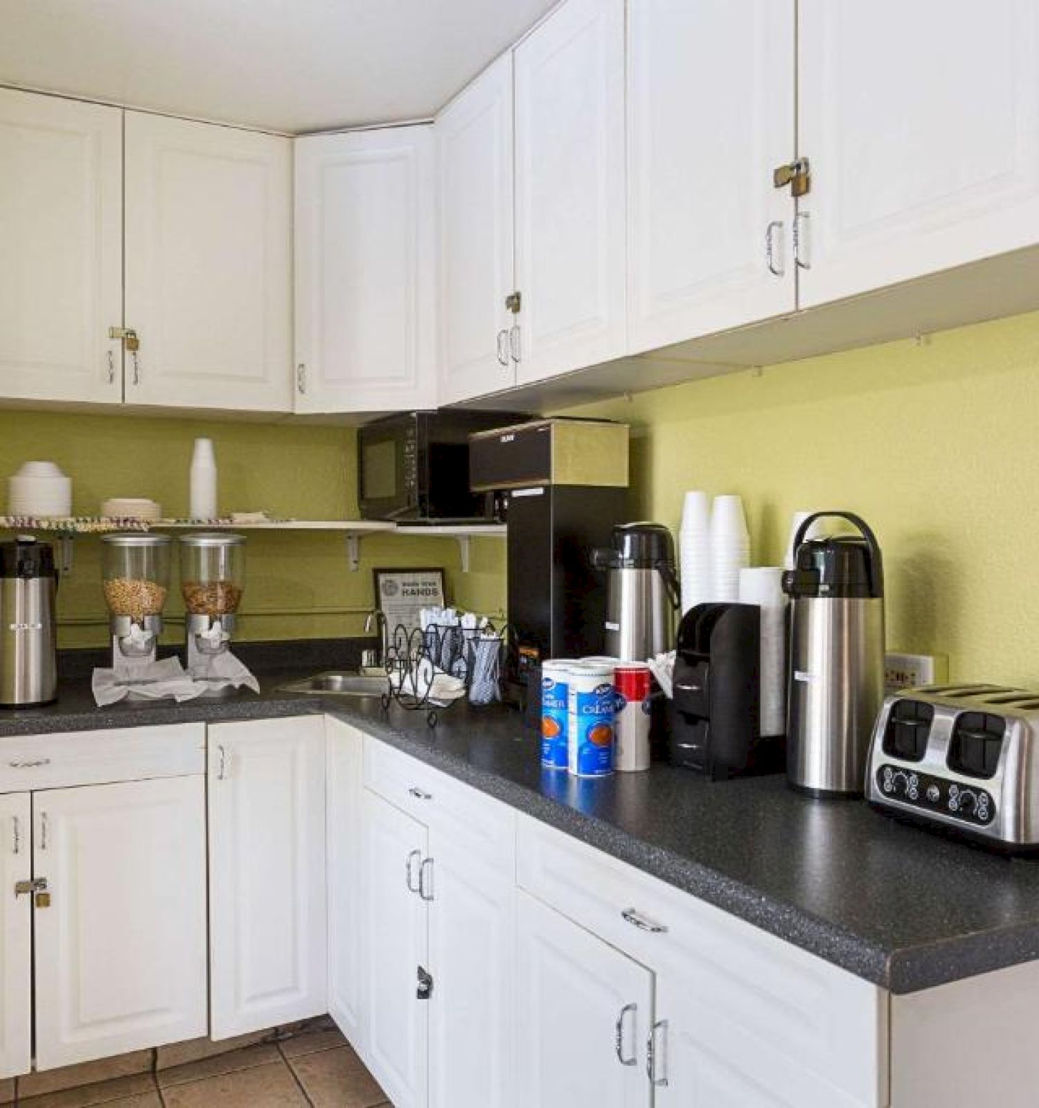 A small kitchen setup with white cabinetry, a coffee station, a toaster, and various kitchen supplies on the countertop ending the sentence.