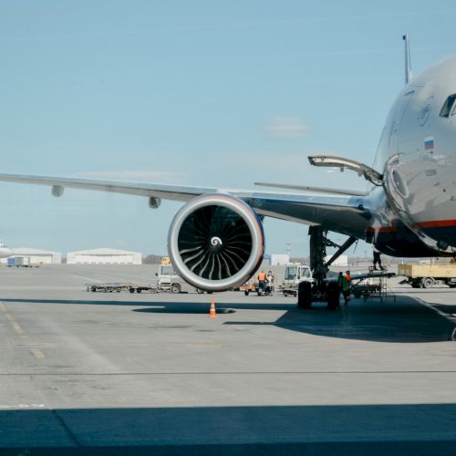 A large commercial airplane is parked on the tarmac at an airport, with some ground vehicles and buildings in the background.