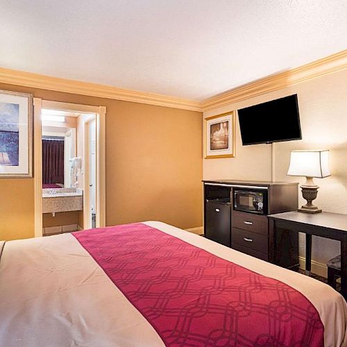 A neatly decorated hotel room with a bed, two lamps, a TV, a desk, and a microwave. A bathroom is visible through an open door.