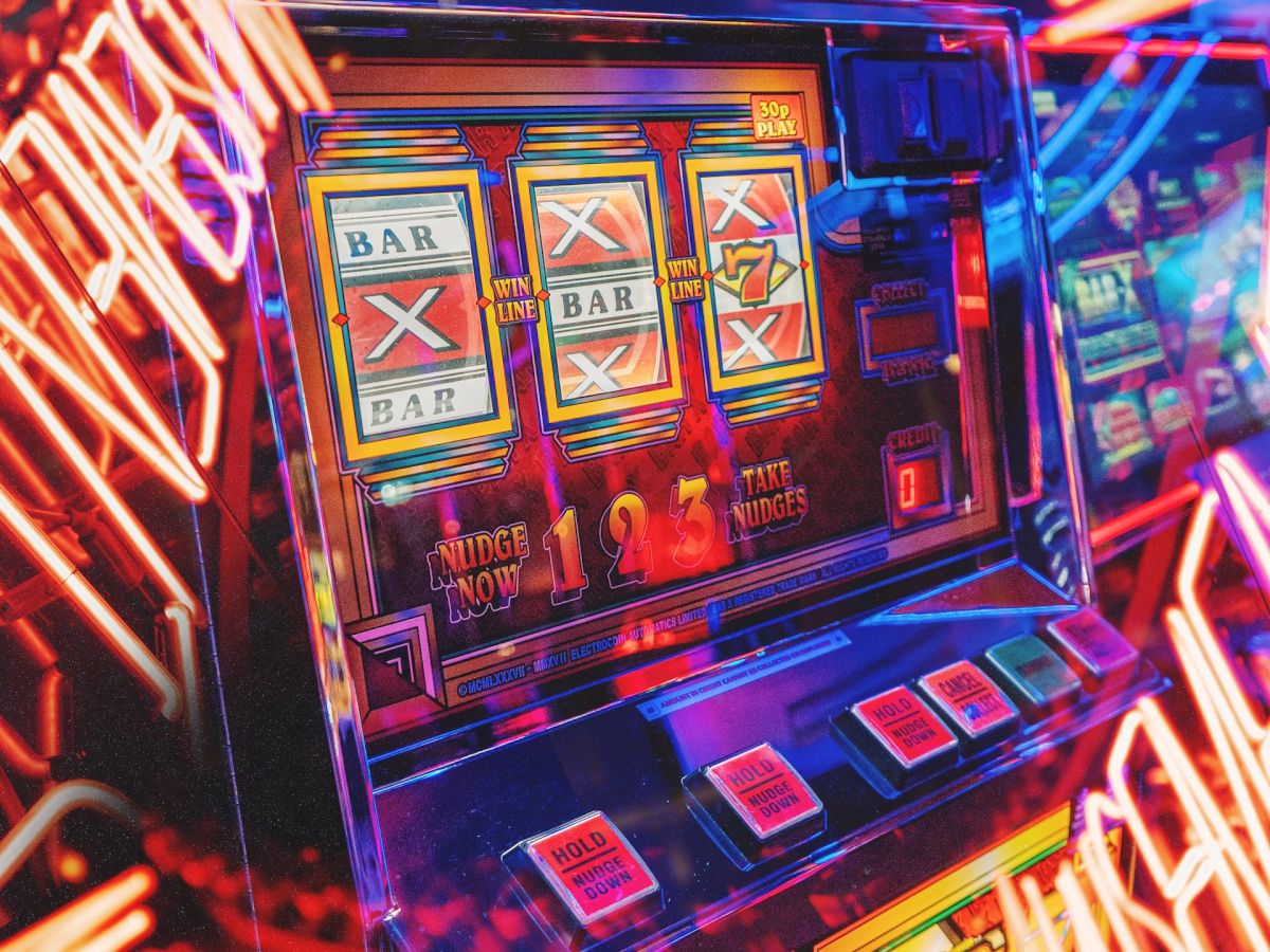 The image shows a vibrant, neon-lit slot machine in a casino, with illuminated lines and patterns surrounding it.