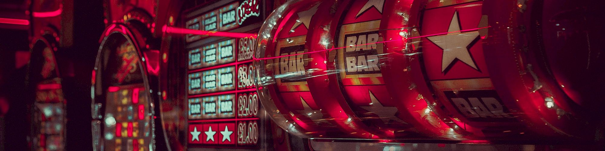 A row of illuminated slot machines in a dimly lit casino, with red lighting and reflections creating a vibrant and lively atmosphere that invites gameplay.