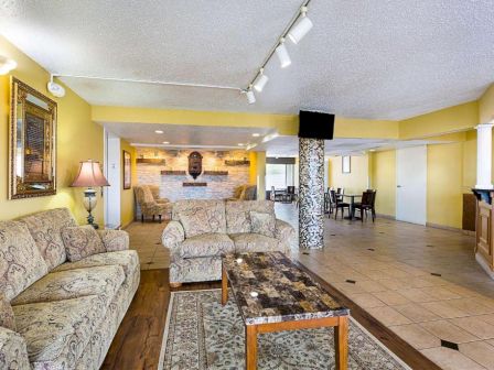 A spacious living area with yellow walls, patterned couches, a marble coffee table, a floor lamp, and a wall-mounted portrait in the background.