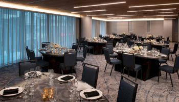 A formal dining room with round tables set for an event, featuring chairs, silverware, glassware, centerpieces, and dim lighting.