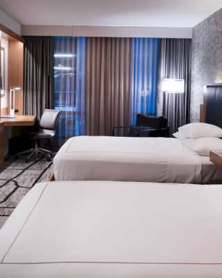 A modern hotel room features two neatly made beds, a large wall-mounted TV, a desk, and ambient lighting.