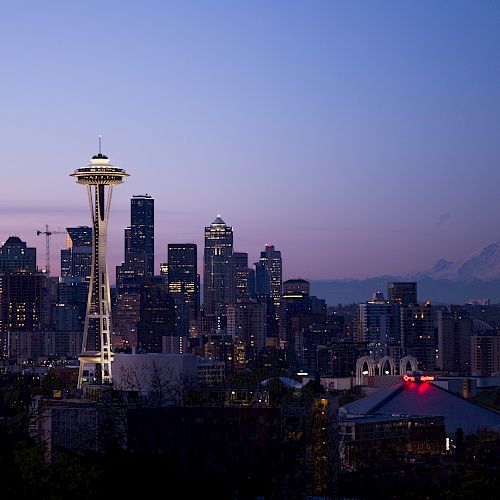 The image depicts the Seattle skyline at dusk with the Space Needle prominent, and Mount Rainier visible in the background.