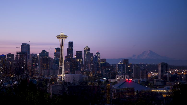 This image shows the skyline of Seattle, Washington, featuring the Space Needle and Mount Rainier in the background during twilight.