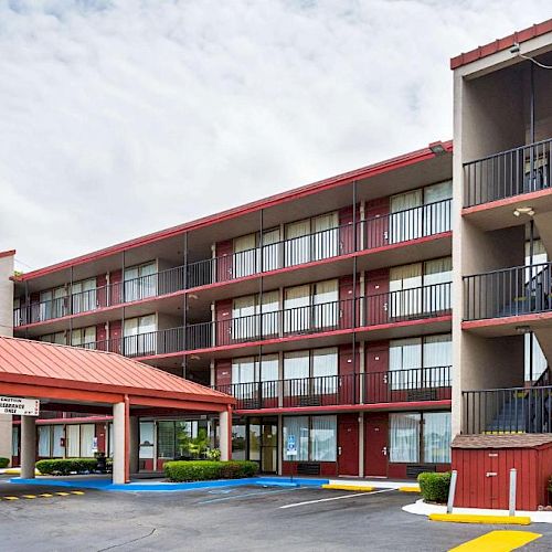 The image shows a multi-story motel building with exterior corridors and staircases, and a covered entrance area, surrounded by a parking lot.