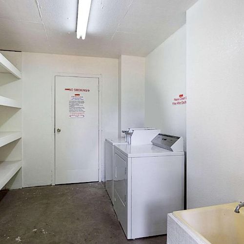 The image shows a laundry room with shelves on the left, a washer and dryer in the center, a sink on the right, and a door in the background.