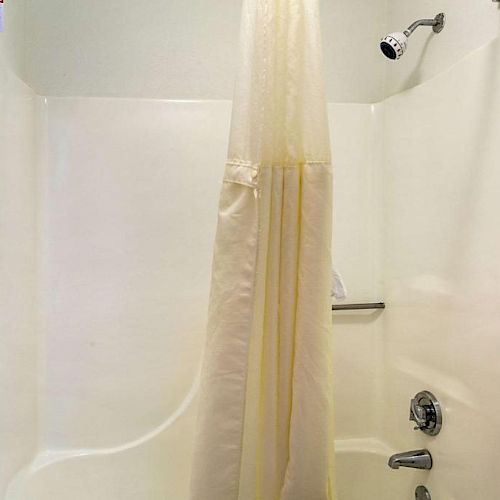 The image shows a white bathroom with a bathtub and shower, a shower curtain, and fixtures including a showerhead and faucet handle.