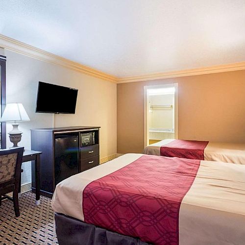 A hotel room with two double beds, a TV, a desk, chair, lamps, and a mirror; in a neutral tone setting.