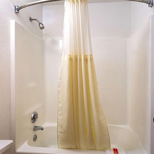 A bathtub with a shower curtain closed halfway, a showerhead, a faucet, and a soap holder, seen from the doorway.